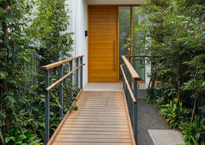 Modern home entrance featuring a wooden wheelchair ramp for easy access, surrounded by greenery. Designed for convenience and inclusivity, blending functionality with minimalist aesthetics.